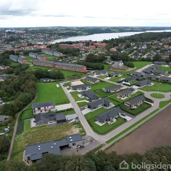 Byområde set fra luften med moderne huse arrangeret i en grøn bebyggelse. I baggrunden ses en stor flod omgivet af skov og en tættere bybebyggelse.