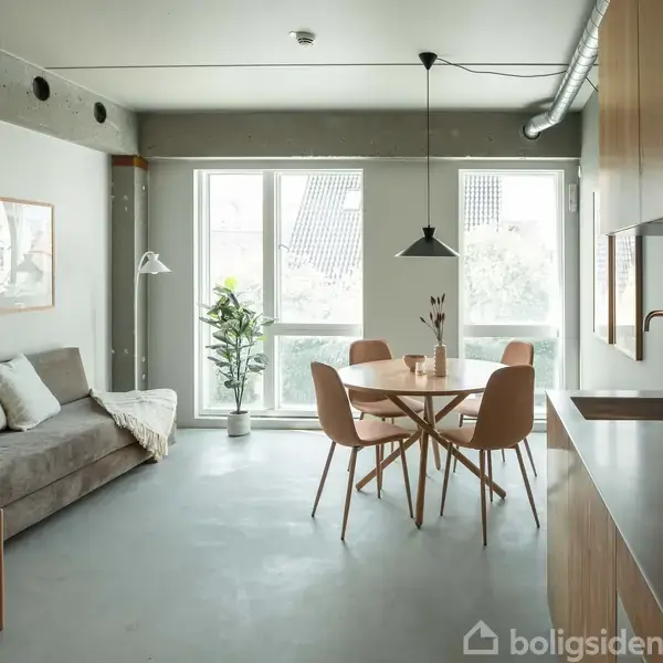 En moderne stue viser en grå sofa med puder ved siden af et rundt spisebord med stole midt i rummet. Store vinduer slipper lys ind, mens en plante står ved siden af bordet.