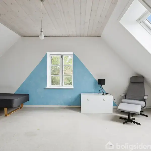 Et lyst loftværelse med en grå sofa til venstre og en grå lænestol med fodskammel til højre. En blå trekant-malet væg har et centralt vindue.