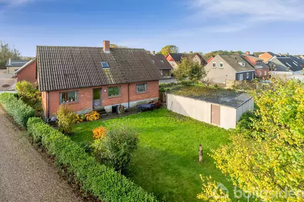 Et rødt murstenshus med skråtag står ved siden af en garage og en grøn have. Hække omkranser grunden, og huset er placeret i et villakvarter.