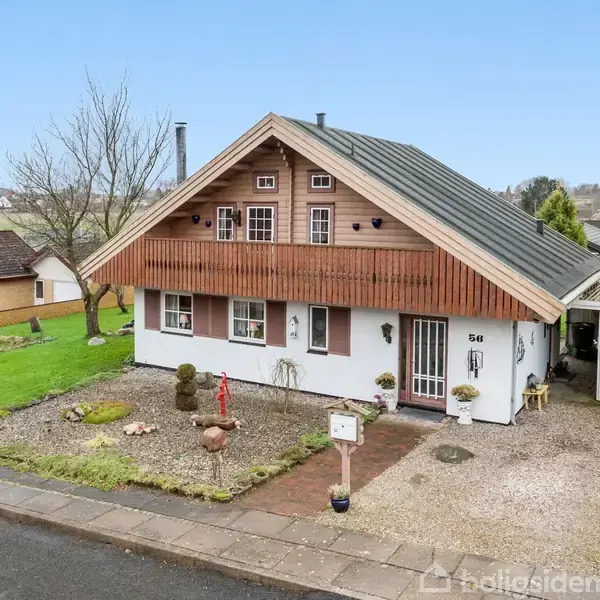 Hus med skråt tag og trægavl står i en velholdt forhave med grus og små buske, omgivet af en rolig villavej. Husnummeret 58 vises ved husets indgang.