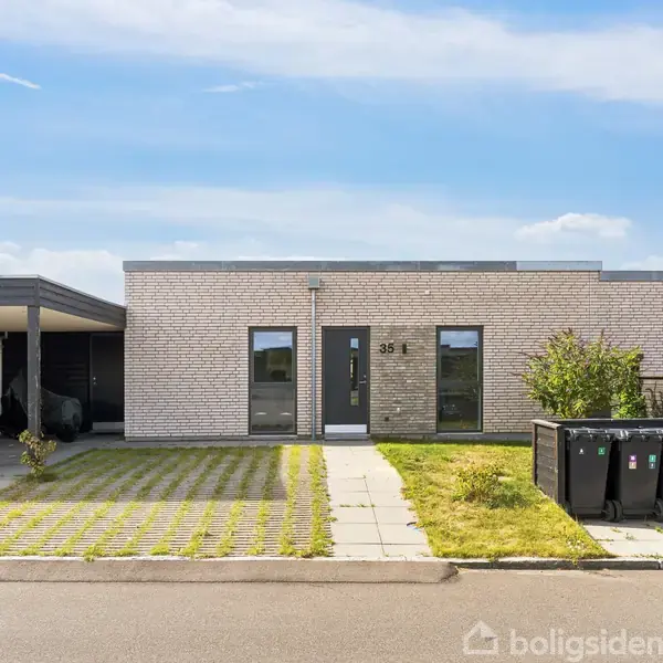 En enkel, moderne etplanshusteglvilla med to vinduer og en dør i midten. Husnummeret "35" står ved døren. Foran er der en flisebelagt gang og en græsbelagt indkørsel.