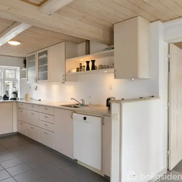 Et moderne køkken med hvidt køkkenskab og skuffer. Midtpunktet er en hvid bordplade med integreret vask. I baggrunden ses et stort vindue, der giver naturligt lys.