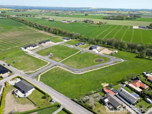 En nyudviklet boligområde under opbygning med flere byggegrunde og enkelte huse langs veje, omkranset af frodige marker og åbent landskab. Ingen tekst er synlig på billedet.