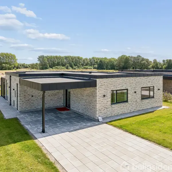 Fladt taghus med moderne design står i et åbent område. Mursten i lyse nuancer præger facaden. Omkringliggende græsplæne og flisebelagt indgangssti kompletterer udseendet.
