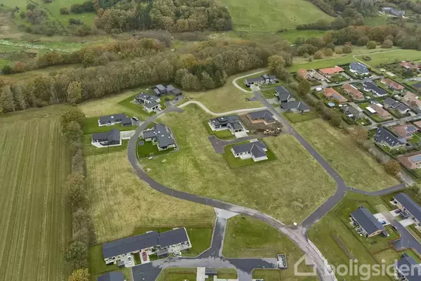 Beboelseshuse spredt ud over et grønt landskab. Husene er placeret langs snoede veje. Omgivelserne inkluderer marker og skove i baggrunden.