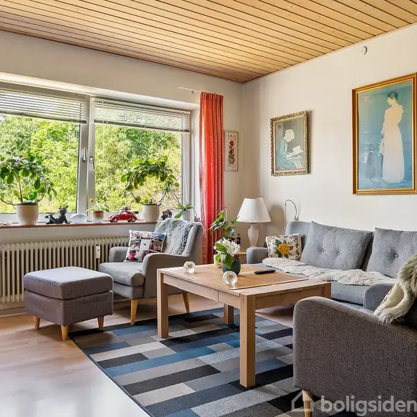 Stue med gråt sofasæt placeret på mønstret tæppe; sofabord med dekorationer. Store vinduer med planter og lysindfald. Væggene har kunstmalerier, og gardinerne er røde med lyse træpaneler.
