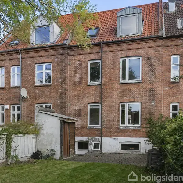 Bygning står stille. Rødt murstenshus med flere vinduer og tagvinduer. Omgivet af en velholdt have med grøn græsplæne og nogle træer.