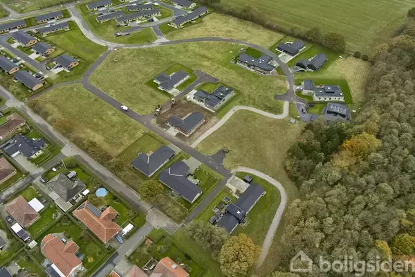 Nybyggerkvarter set fra luften viser flere moderne huse, spredt blandt grønne græsarealer og snoede veje, omgivet af træer og tilstødende beboelsesområde.