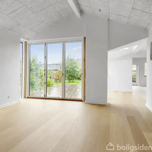 Rummet har store glasdøre, der åbner ud til en have. Lyse parketgulve og hvide vægge præger indretningen, mens loftet har akustikplader. Rummet er lyst og moderne med højt til loftet.