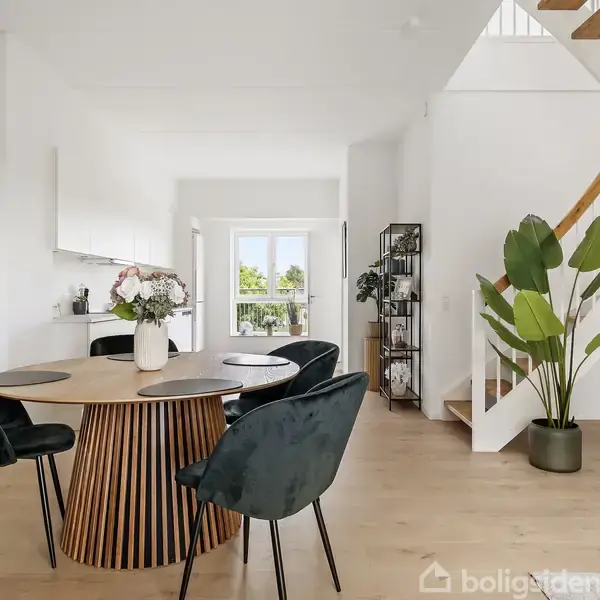 Stor, flisebelagt tagterrasse omgivet af metalhegn. Udsigt over et beboelsesområde med flere bygninger i horisonten under en klar, blå himmel.