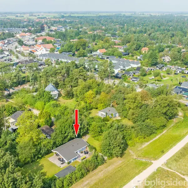 Huset peger nedad med en rød pil, omgivet af træer og buske. Det ligger i udkanten af en beboelsesområde med mange andre huse og grønne områder i forgrunden.