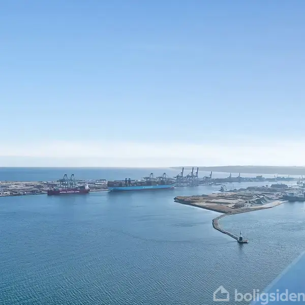 Havnene strækker sig langs kystlinjen, mens kraner står stille i baggrunden. Den blå himmel og roligt hav omgiver området, set fra en høj udsigtsposition.