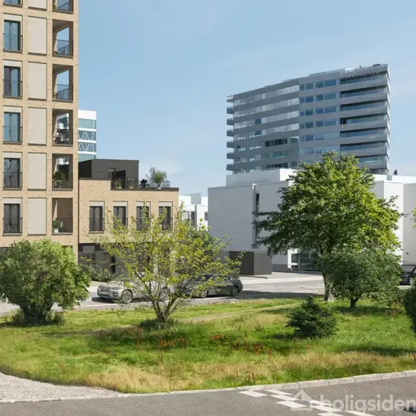 En murstensbygning står stille i en moderne bykontekst omgivet af frodige træer og græs. Biler er parkeret langs vejen foran bygningen, mens en høj bygning ses i baggrunden.