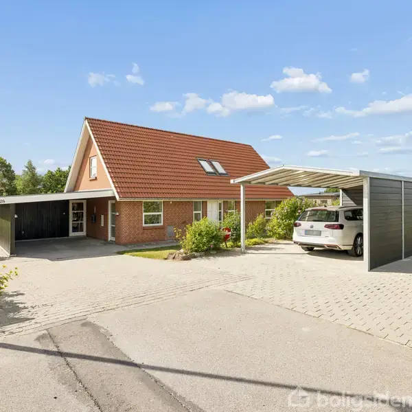 Et rødt murstenshus med rødt tegltag står stille i en fredelig parcelhuskvarter. Ved siden af er en carport med en parkeret hvid bil. Skyfri himmel i baggrunden.