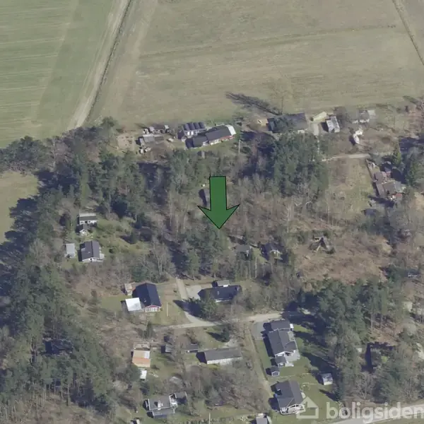 Grøn pil peger på et hus i skovklædt område med spredte boliger. Omgivet af træer og åbne marker.