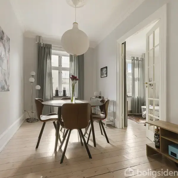 Et spisebord med seks stole står i centrum af et lyst rum med trægulv. En stor loftlampe hænger over bordet. Vinduet har grå gardiner, og der hænger billeder på væggene.