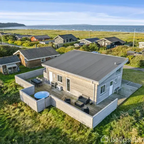 Et enkelt træhus med terrasse er placeret tæt på kysten. Huset har en udendørs terrasse med siddeområde og spabad, omkranset af græs og andre sommerhuse.