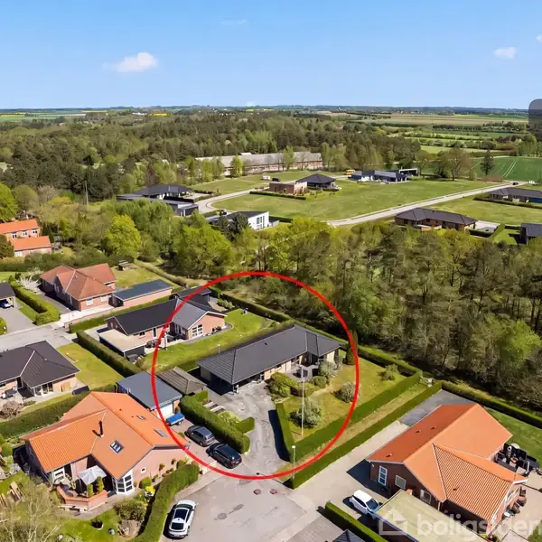 En cirkel markerer en enkeltstående bygning i et parcelhuskvarter med grønne områder og skove i baggrunden. Teksten "Visualisering" ses øverst i højre hjørne.