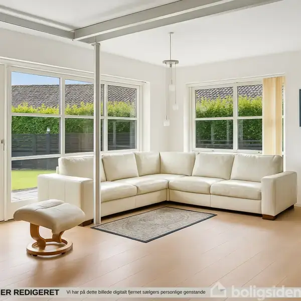 Hvid sofa står i hjørnet af en lys stue med store vinduer. En skammel er tæt på, og en kommode står ved siden af. Kunst hænger på væggen.
DETTTE BILLEDE ER REDIGERET Vi har på dette billede digitalt fjernet sælgers personlige genstande.