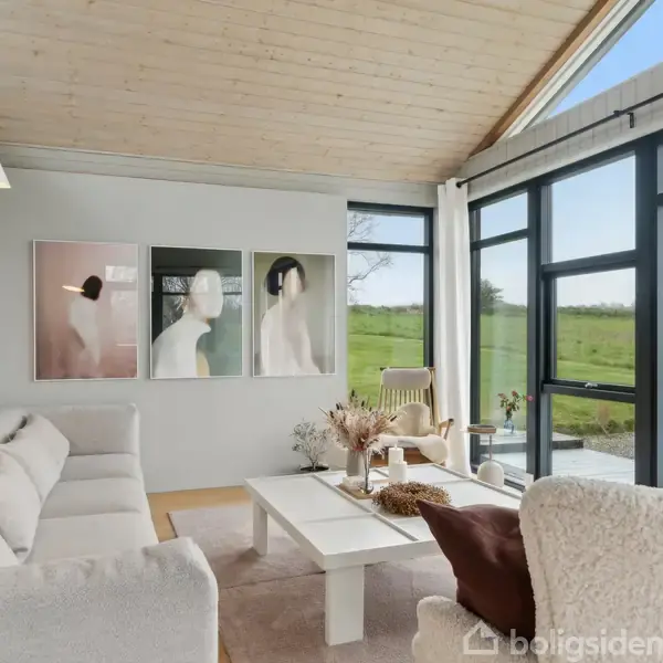 Et moderne køkken med integreret spiseområde; rund sort bord med vase og stole; lyst rum, floral vægdekoration; køkkenø med hængende lamper, hvide skabe og indbygget apparat.