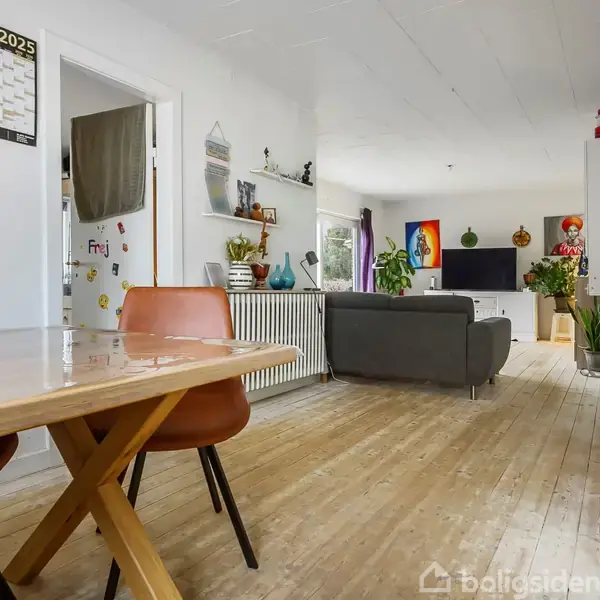 Et spisebord med brune stole står i et rum med trægulve; en sofa orienteret mod et TV i en lys stue med planter og dekorationer. Kalenderen viser "XXL 2025".