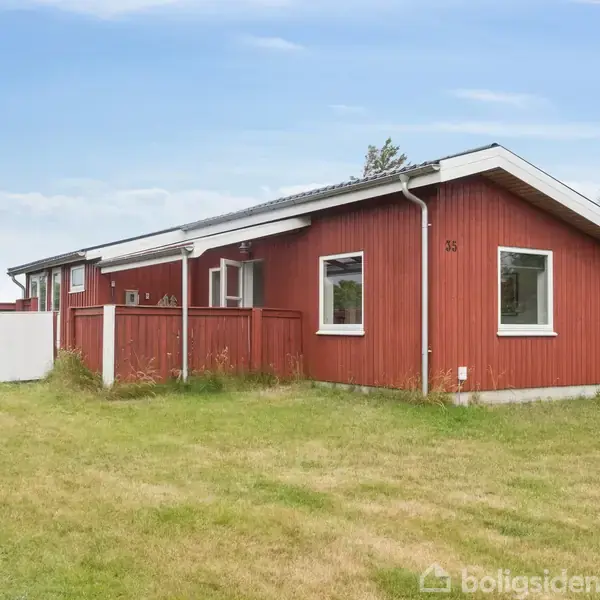 Rødt hus med hvide kanter står på en grøn græsplæne. Der er træer i baggrunden, og himlen er blå med lette skyer. På husets side står tallet "35".