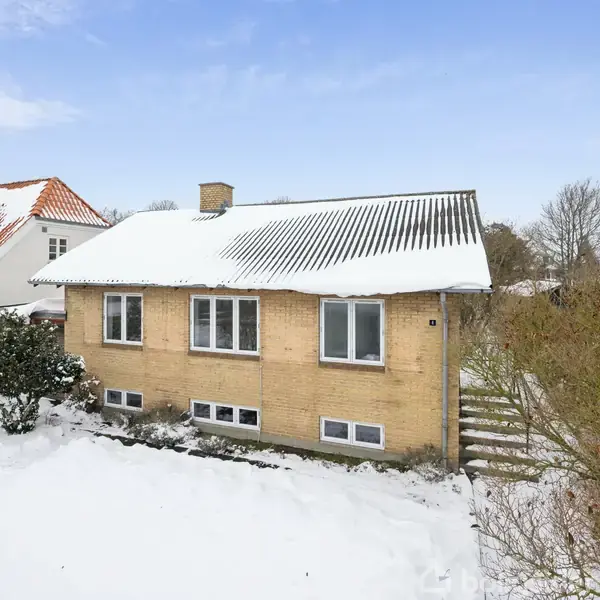 Et køkken med grå skabe og skuffer omgiver en vask til venstre og en komfur til højre. Baggrunden har et vindue med udsigt til træer og himmel.