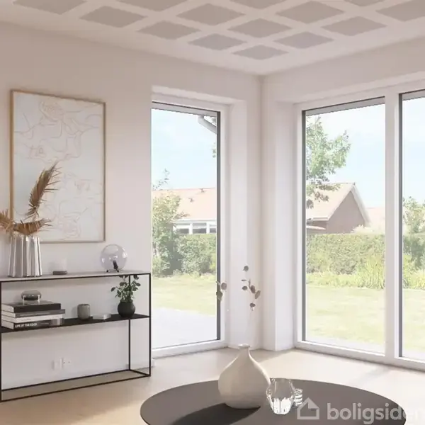 En stue med lyse vægge har et minimalistisk bord med vaser og dekorationer. Store vinduer giver udsigt til en grøn have og et hus i baggrunden. Ingen tekst synlig.