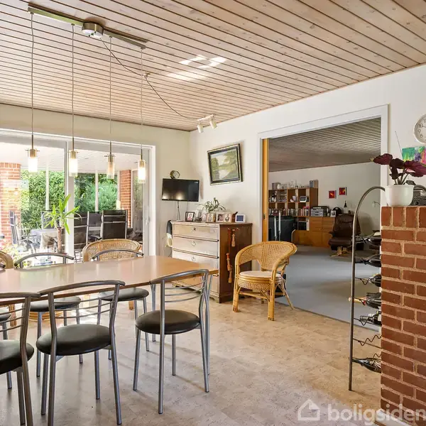 Spisebord med fire stole, aktion ingen, kontekst i en lys stue med trægulve, sofa i baggrunden, store skydedøre til en terrasse med havemøbler.