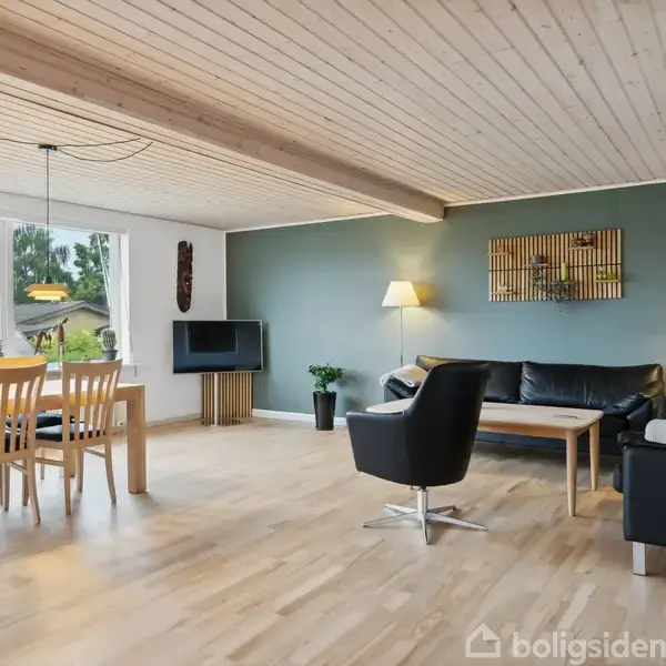Stue med spisebord og seks stole til venstre, en sort lædersofa og lænestol til højre. Lyse trælofter og gulve. Grøn væg med maleri. Store vinduer giver udsigt til have.