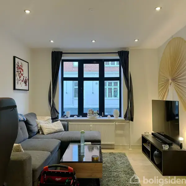 Et sort spisebord med stole omkring står i et rum. På bordet ligger en notesbog og termokander. Vindue med udsigt til bybygning. Vægkunst hænger til venstre.