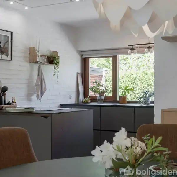 Et moderne køkken med mørkegrå skabe og hvid murstensvæg. På bordet står køkkenredskaber og en plante. Et vindue viser en grøn have. En rund lampe hænger over blomster på et bord.