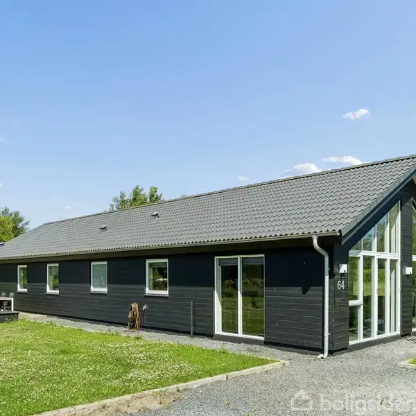 En moderne, sortmalet én-etagers bygning med store glasvinduer står stille i en grøn haveområde med græsplæne og buske under en klar blå himmel. Husnummeret er 64.