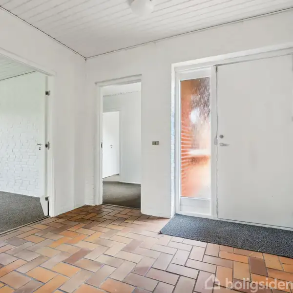 Entré med brunlige klinkegulve, lyse vægge og flere døråbninger. En glasdør leder udenfor. To indvendige døre fører til andre rum i huset.