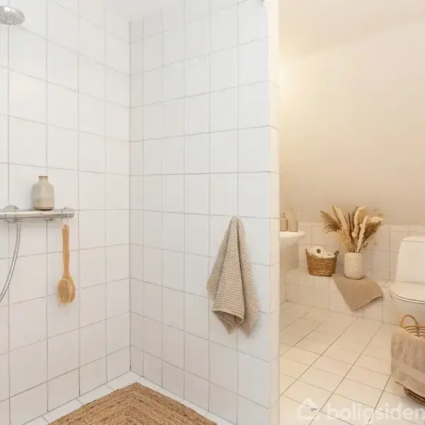 En lys stue med en beige sofa, lavt sofabord og lys trælænestol på et blødt tæppe. Vinduer i skråvæggen lader naturligt lys strømme ind.