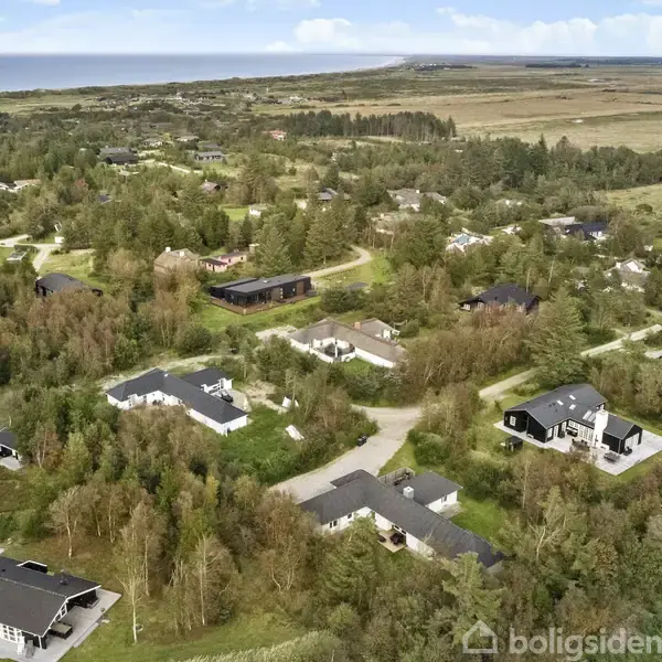 Et boligområde med huse spredt blandt træer nær kysten. Området er omgivet af landskab og marker, med veje der forbinder de enkelte boliger. Kystlinjen er synlig i baggrunden.