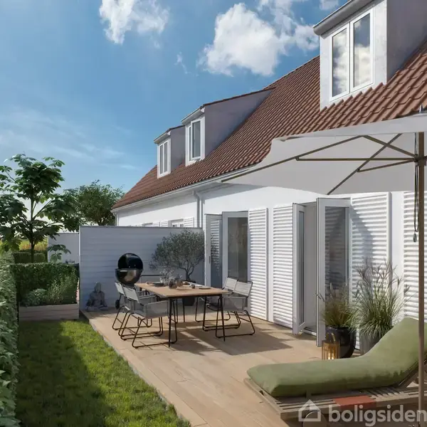 Rækkehus med rødt tegltag og hvide vægge har en terrasse med spisebordssæt, liggestol og parasol. Det ligger i et grønt, landligt område med udsigt til marker.