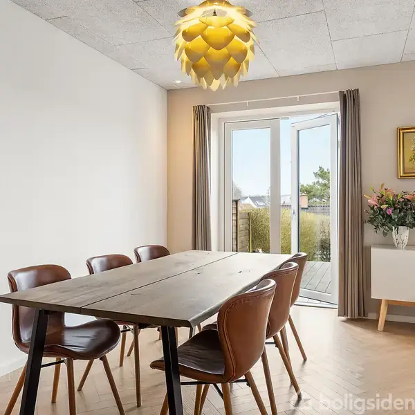Et rektangulært spisebord med seks stole står i en lys spisestue. Bordet er placeret på et trægulv. I baggrunden er der en kommode med en vase fuld af blomster. En stor pendellampe hænger fra loftet. I hjørnet af rummet hænger et maleri. Fransk dør fører ud til en altan med udsigt.