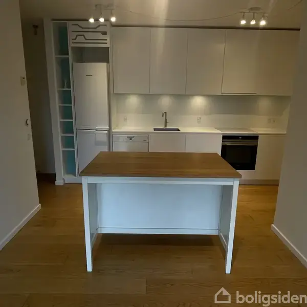 En grøn stol og bord står på en balkon med udsigt over moderne, buede bygninger og en vandkanal i en bydel, mens skyer fylder himlen.