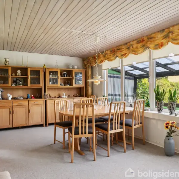 En spisestue med et træbord og otte stole omkranset af glasvægge, der giver udsigt til en have. En skabsvæg med pyntegenstande ses i baggrunden.