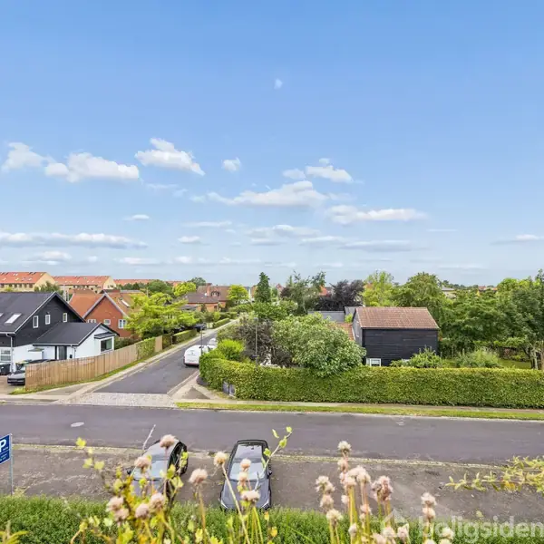 Stue med sofa og lænestol ved et sofabord, i aktion med et rødt fad som dekoration. Konteksten er en lys stue med et spisebord ved vinduet, udsigt til et boligområde.