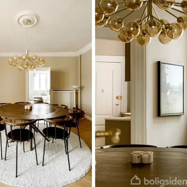 Rundt træspisebord står midt i spisestue, omgivet af seks sorte stole. Over bordet hænger en moderne, gylden loftlampe. Rummet fremstår lyst med lyse vægge og vinduer.