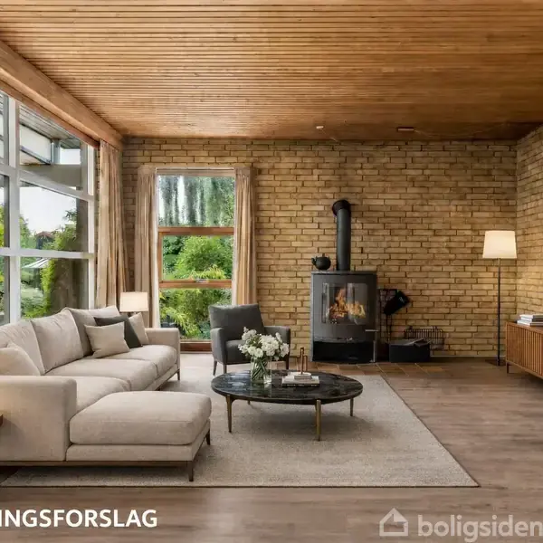 Stue med beige sofa, rund sofabord og brændeovn. Store vinduer slipper naturligt lys ind. Væggene er af mursten, og der står "INDRETNINGSFORSLAG" i nederste hjørne.