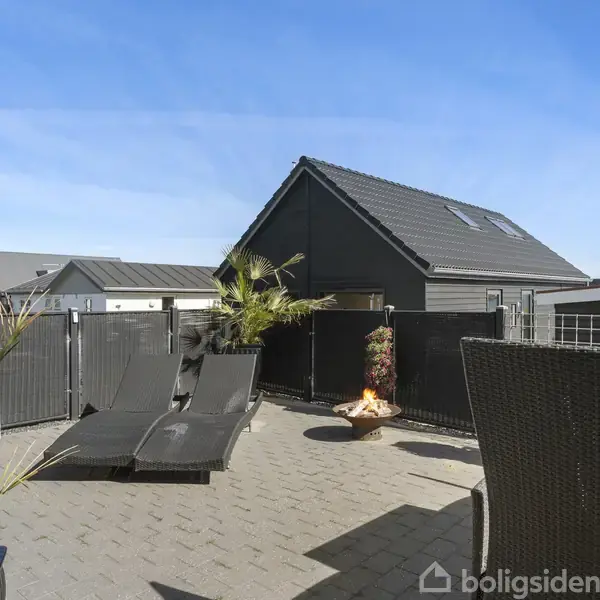 En entré med hvidt klædeskab, jakker hænger ved siden af en glasdør. Tre par sko er placeret på gulvet, og der er udgang til en terrasse.