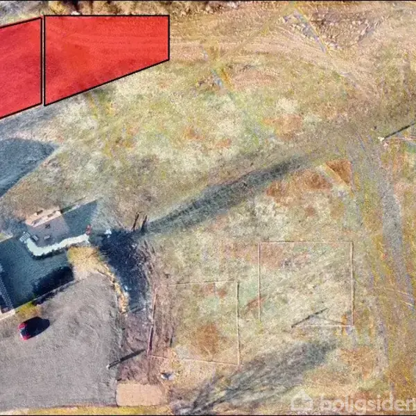 To parceller markeret med rødt, viser to byggegrunde. En bygning med sort tag ses ved siden af en parkeret bil på grusvej. Omgivelserne er åbne grønne områder.