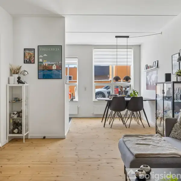 Bygning med murstensfacade med flere vinduer, hvor et skilt i et af vinduerne siger "Til salg". Placering ved en vejkant med flisebelægning, postkasser ved siden af en dør.