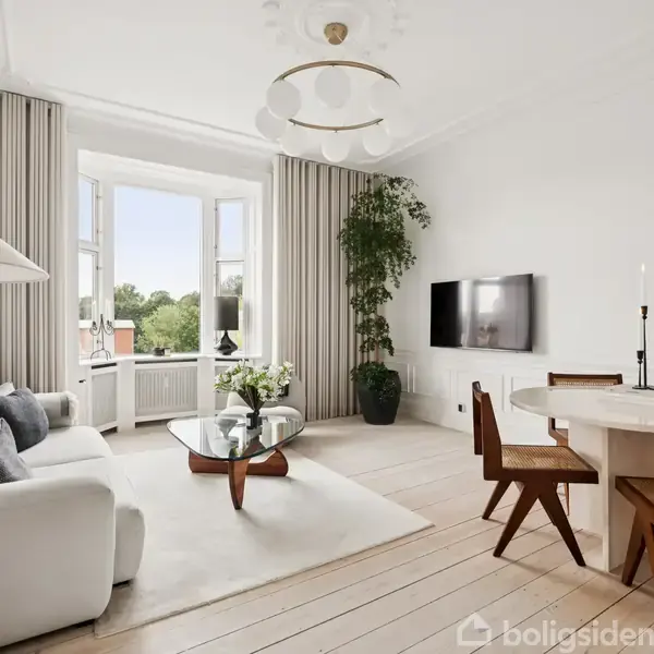 Stue med hvid sofa og sofabord i midten, ved siden af et rundt spisebord med fire stole. Et stort vindue åbner op mod grøn udsigt.
