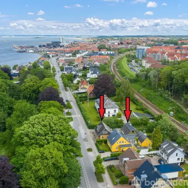 To huse er markeret med røde pile. Handlingen er udefineret. I konteksten ses en kystnær by med veje, jernbanespor, træer og flere bygninger langs vandet.