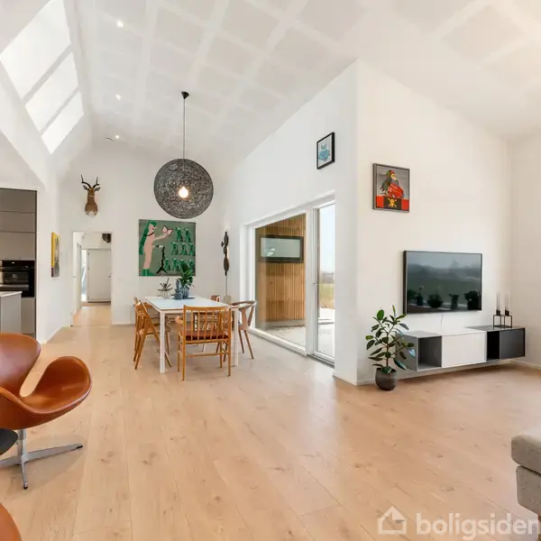 Moderne husfacade med runde vinduer i træbeklædning. To store glasdøre åbner til en indgang. En dekorativ kugleformet skulptur står til højre. Omkringliggende have med flisebelagt sti.